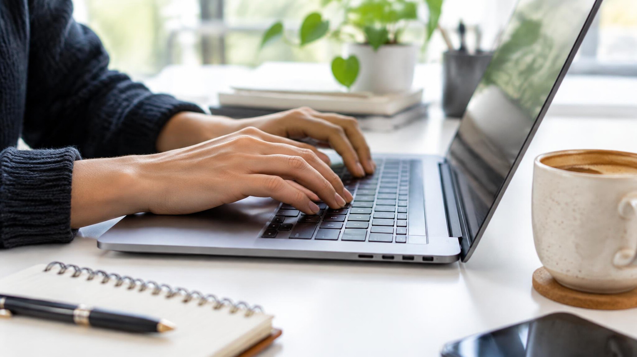 Hands typing on a laptop at a desk